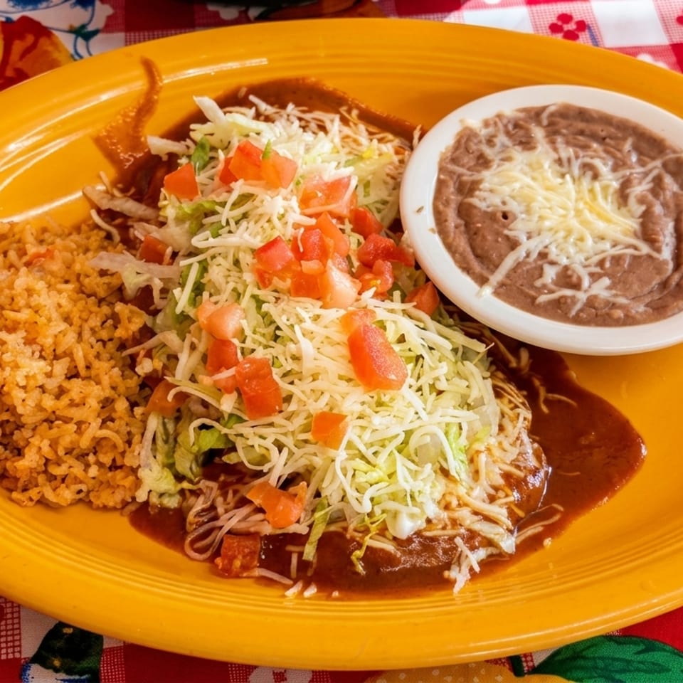 A vibrant yellow plate holds enchiladas topped with lettuce, tomatoes, and cheese, alongside rice and refried beans.