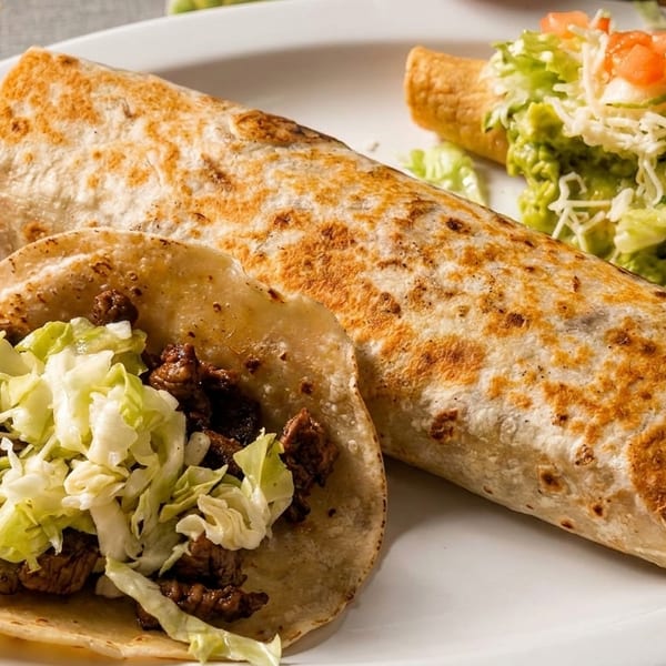 A plate with a large burrito, a beef taco with lettuce, and a taquito topped with guacamole.